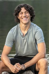 Jaycee Williford, a marine biology student, sits smiling into the camera wearing black shorts and a grey tshirt.