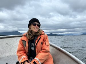 A woman wearing an orange life jacket sits on a boat on a large lake.