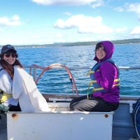 Two people sit on a boat with calm blue sea in the background.