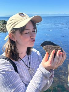 Lauren stands on a beach holding a sea organism.