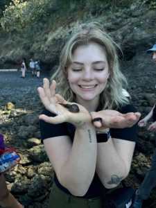 Maddy Glasser holds a small shell and crab in her hands on a beach