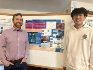 Justin Kwok stands next to another person in front of a research poster