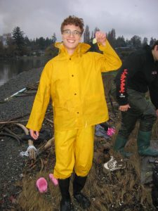Spencer Hill holding a sea organism in a beach, dressed in yellow rainwear