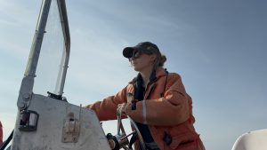 Kylie West pictured from below operating a boat while wearing an orange life jacket