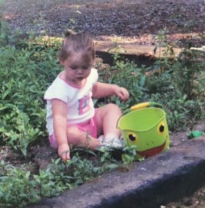 McKayla as a child, sitting in grass with a green bucket.