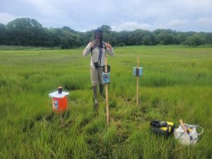 Kathryn stands in a grassy field with research equipment.
