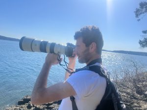 Dylan taking a photo with a long-lens camera overlooking the water