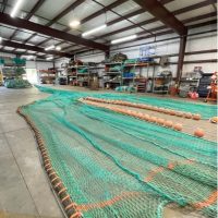 A large and long green net lies on the floor of a warehouse.