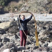 Student holding large piece of kelp on rocky beach
