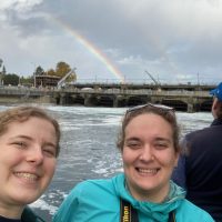 two people in front of dock and rainbow