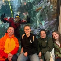 four people in front of aquarium with diver in the tank